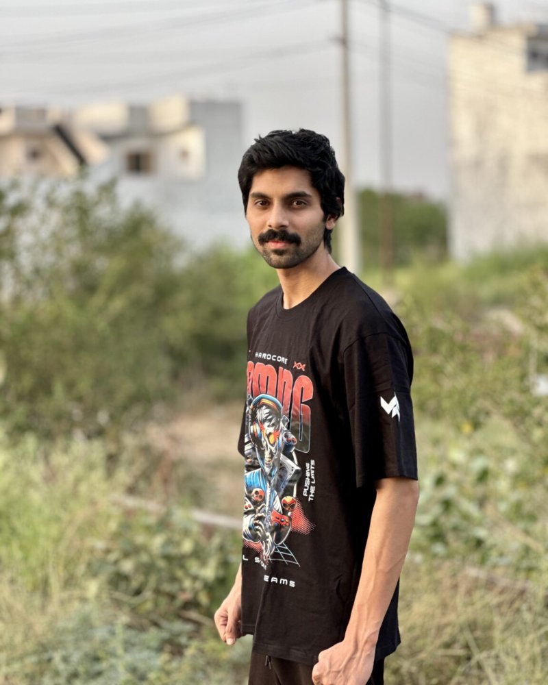 A stylish young man wearing a Swavable black oversized graphic T-shirt with a bold futuristic print, posing confidently outdoors in natural light.